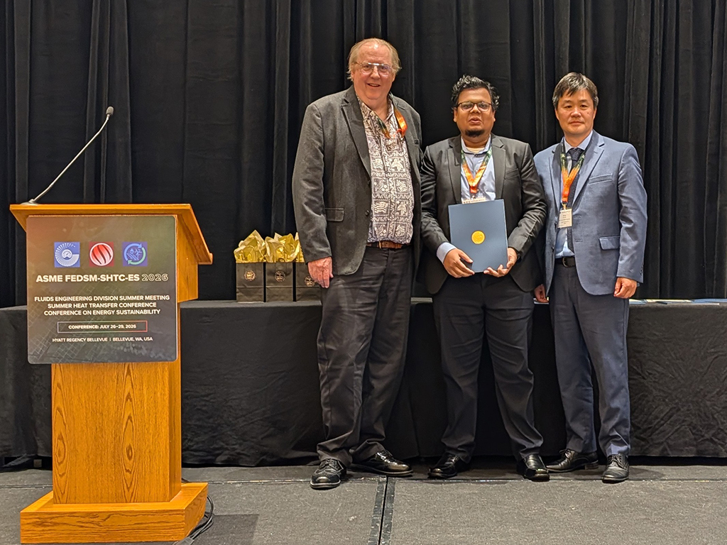 Three men pose onstage at an ASME award ceremony beside a podium and trophy table, smiling proudly in a formal, celebratory setting.
