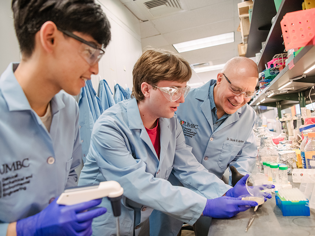 students and professor wearing lab coats with a petri dish in the lab