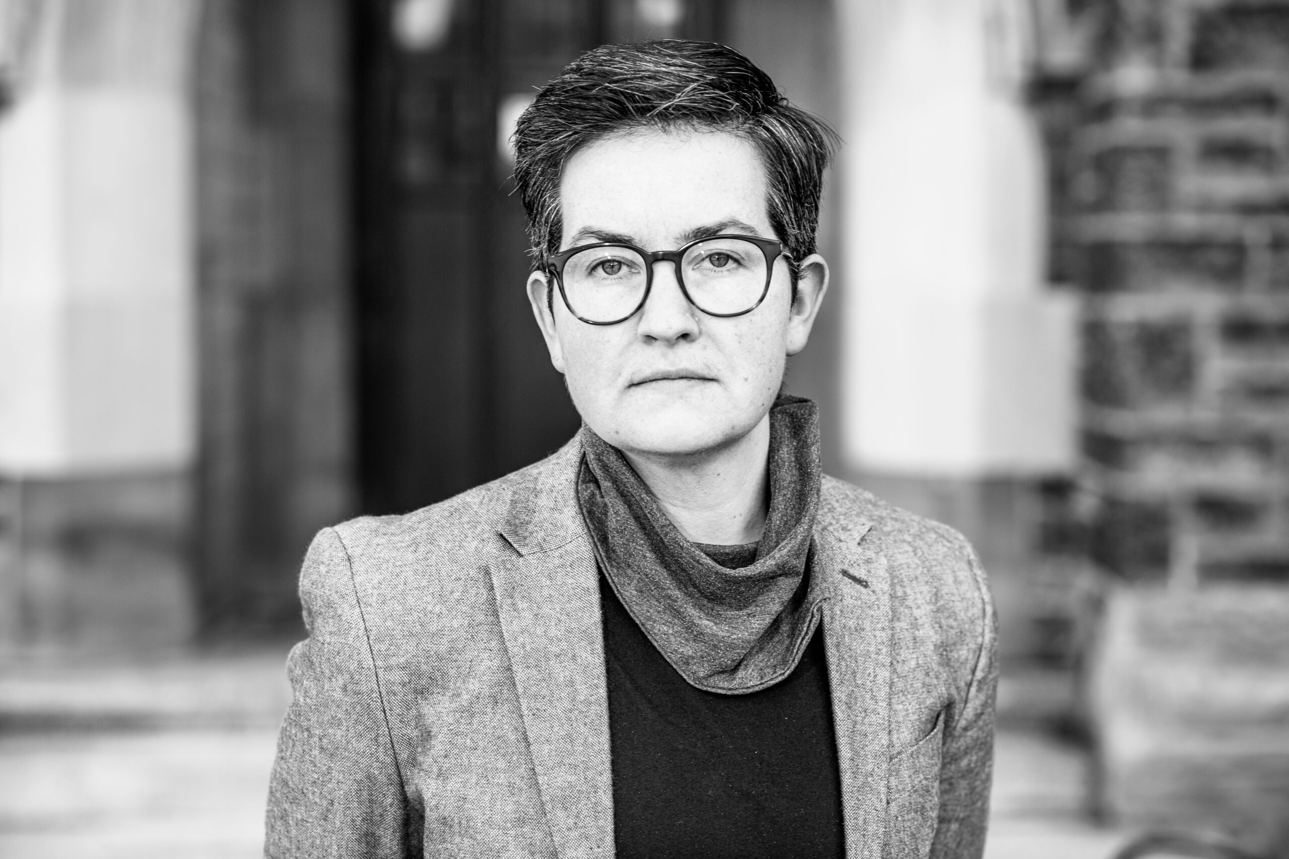 A black and white image of a woman with short hair. She is wearing glasses and a gray suit jacket.