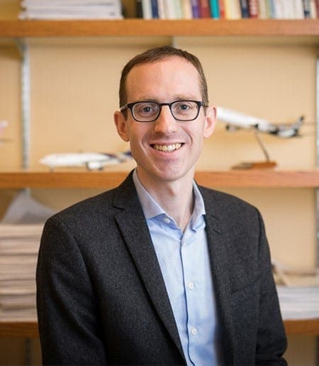 A white man with glasses and a blue shirt is smiling.