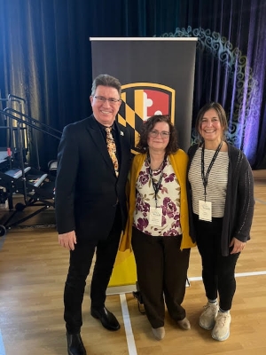 Dr. Karl Steiner, Cathy Manalansan, and Valerie Casasanto stand together, in front of podium with UMBC logo