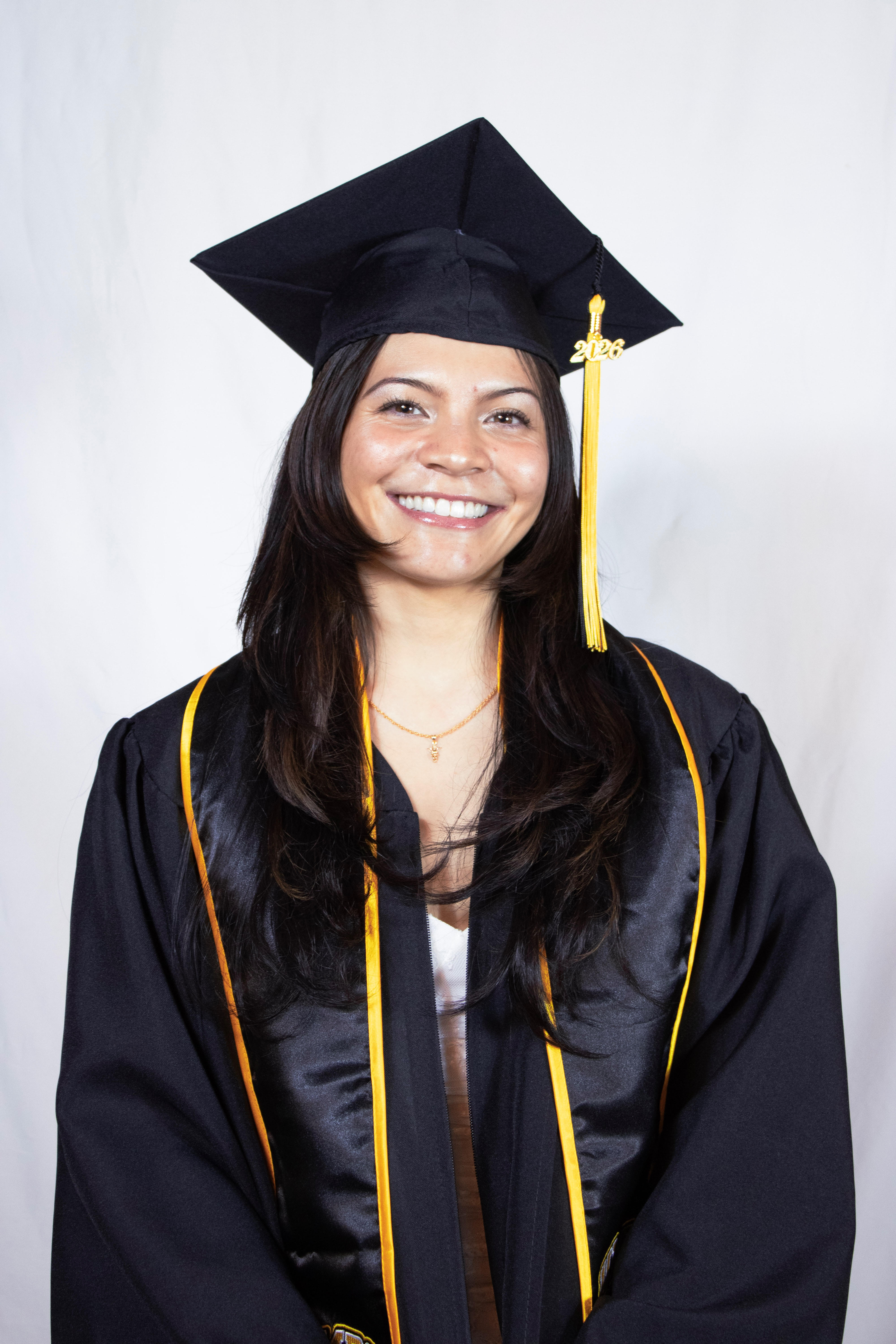 Tristen wearing her UMBC black cap and gown with a gold 2026 tassel while smiling in front of a white background