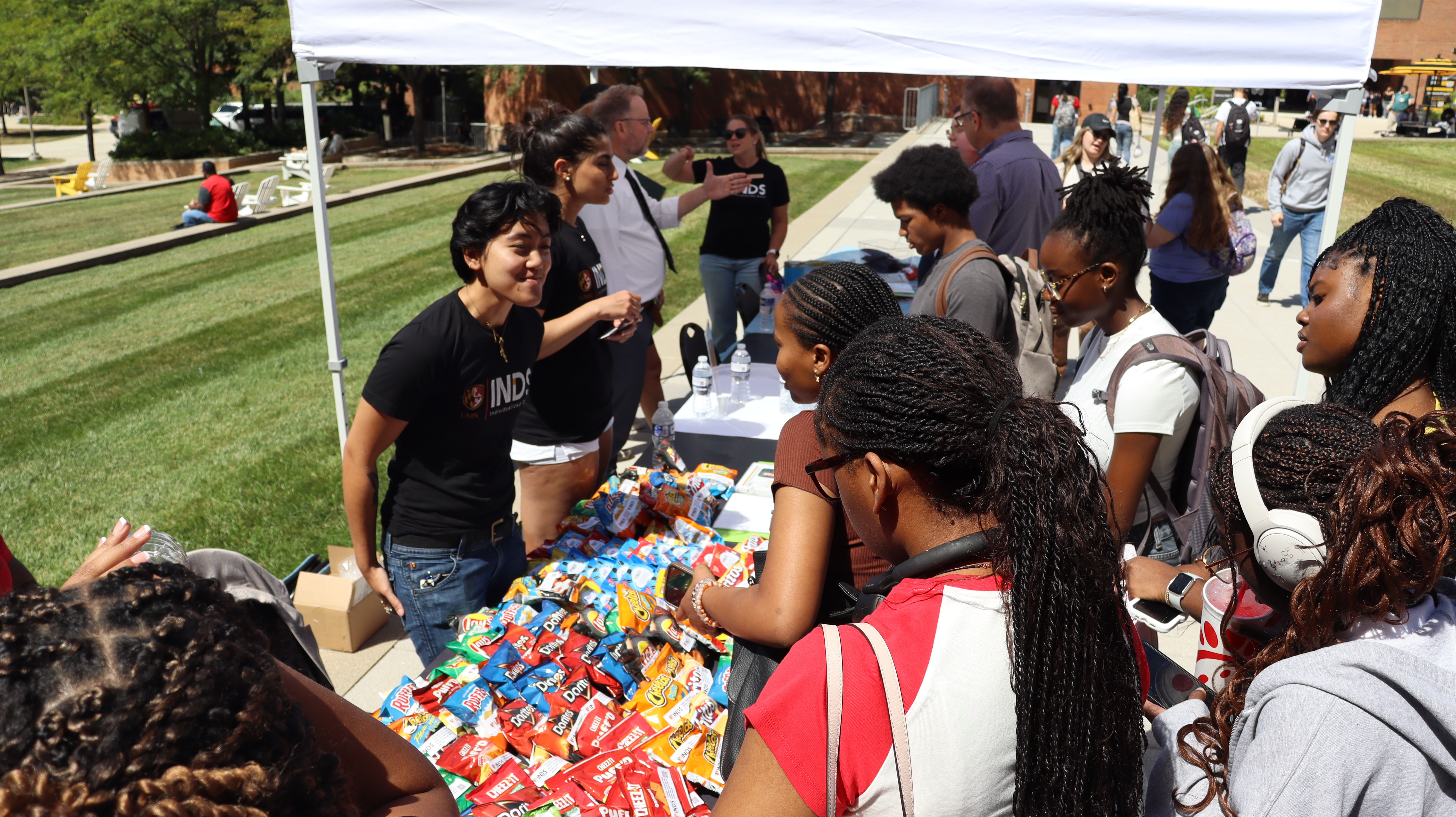 INDS students and team speaking with students about the INDS program outside under a white tent with snacks on the table below