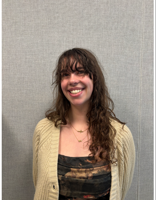 Trilece wearing a yellow cardigan and smiling in front of a gray background.
