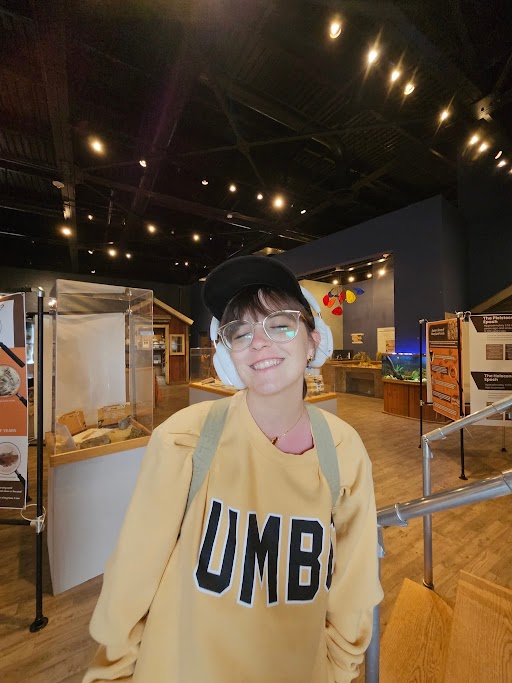Sofia wearing a yellow "UMBC" crewneck and smiling with her eyes closed