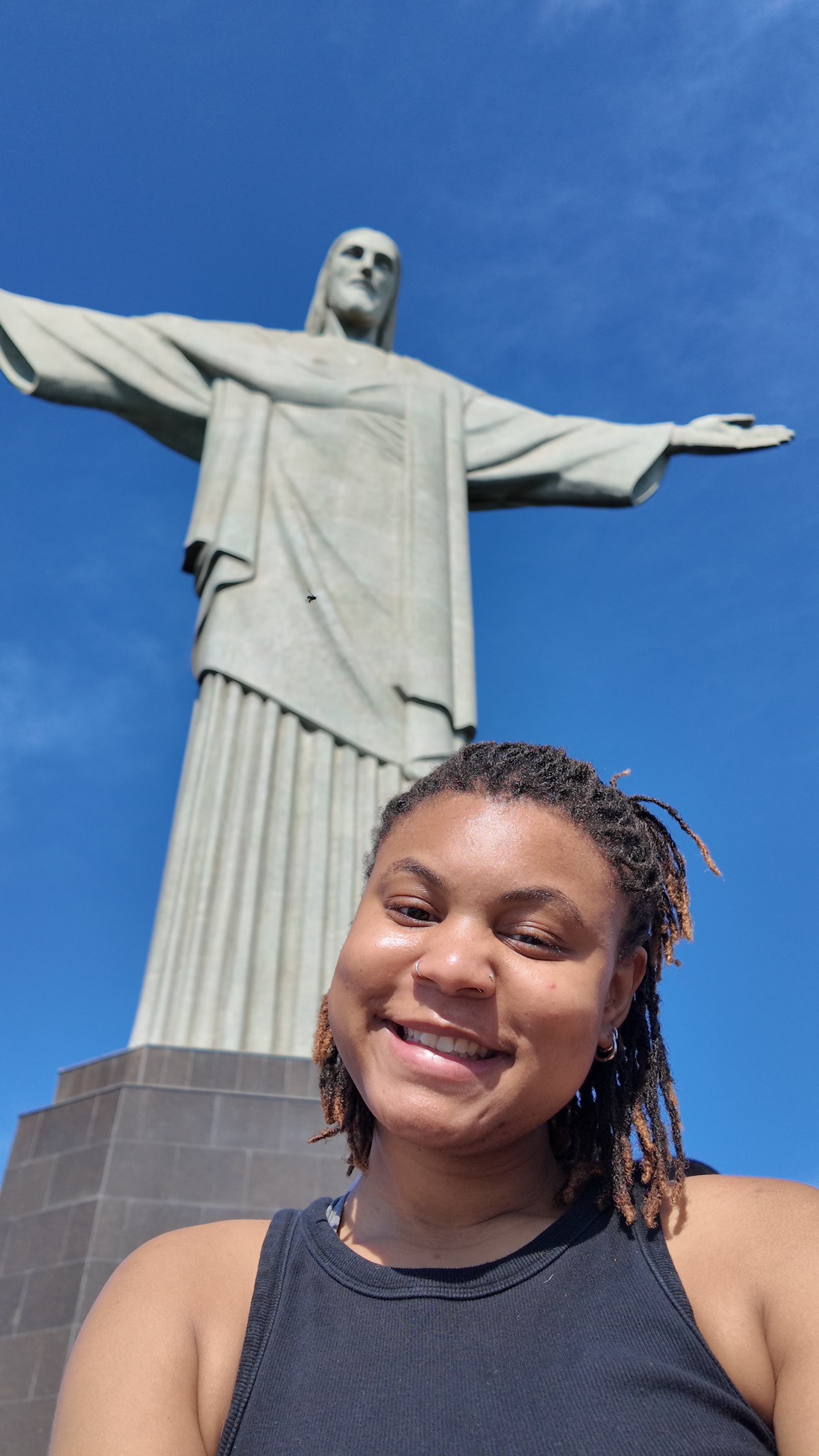 Shania in black top smiling with a white statute with arms open behind Shania