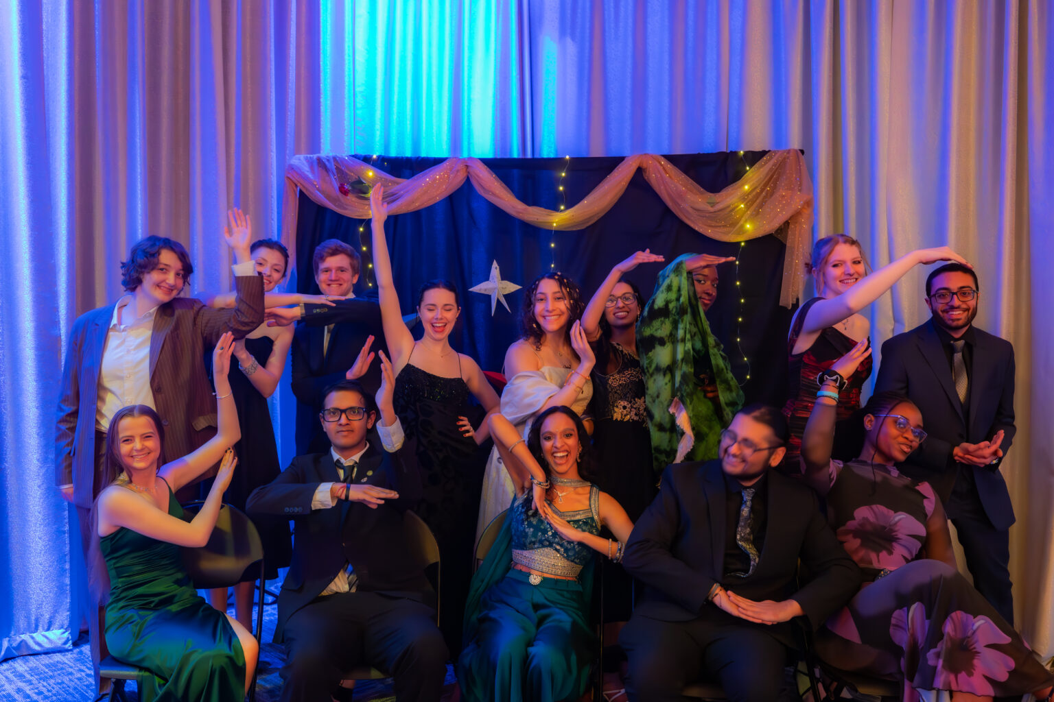 Several students in formal wear pose in front of a dark background with ribbons.