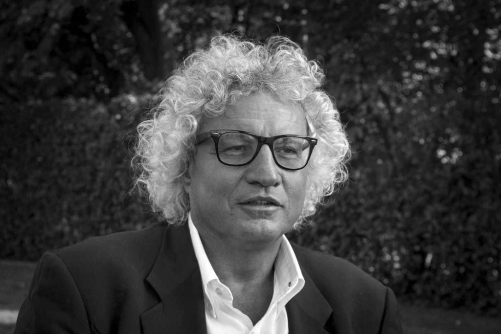 A black and white image of a man with white, curly hair and wearing eye glasses.