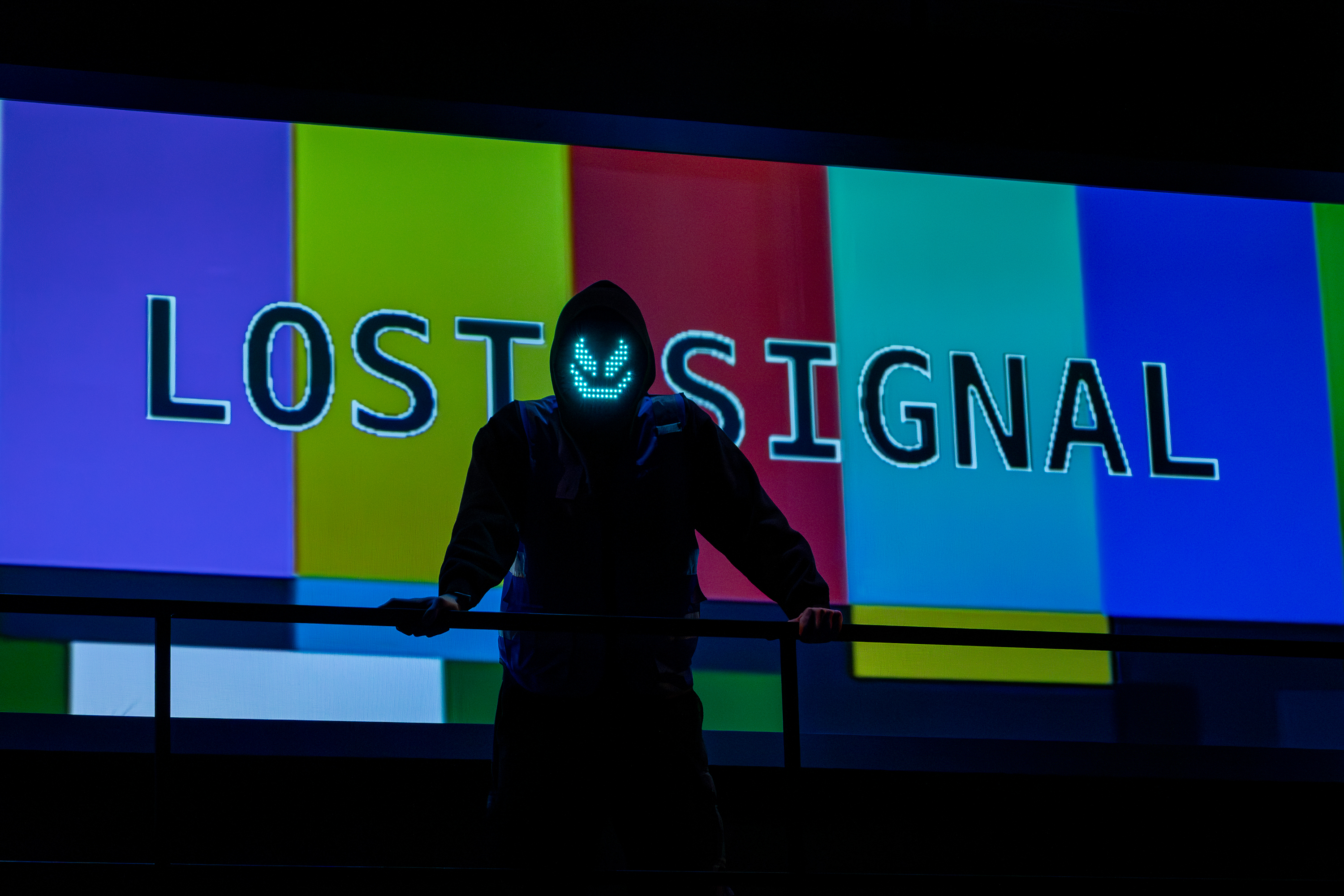 Production photo from User Agreement. A dark figure wearing an ominous electronic mask stands in front of a broadcast screen that reads "Lost Signal".