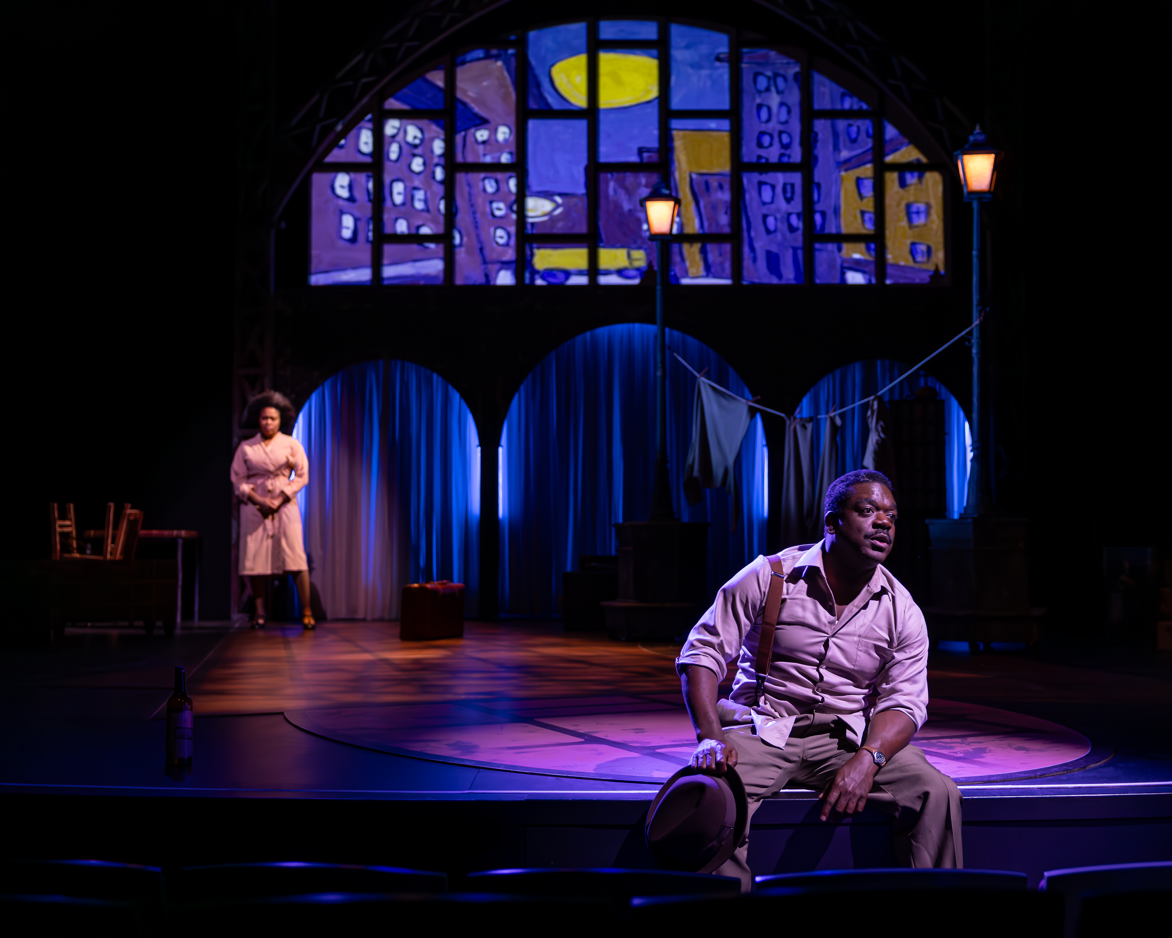 Production Photo from Shakespeare in Harlem. We see Griot upstage, and Simple seated on the edge of the stage looking forlorn.
