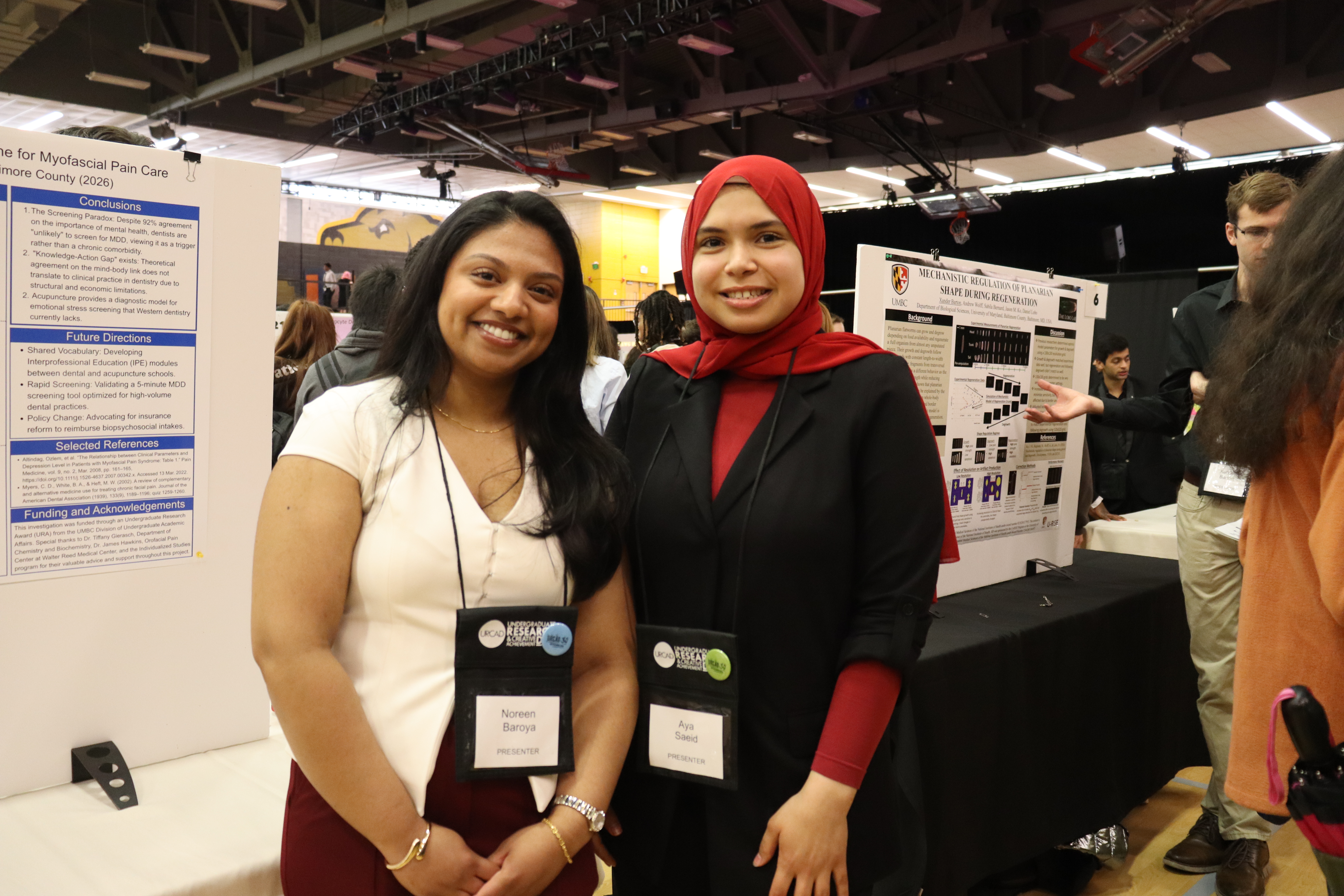 Noreen standing next to fellow INDS student and research poster board, smiling