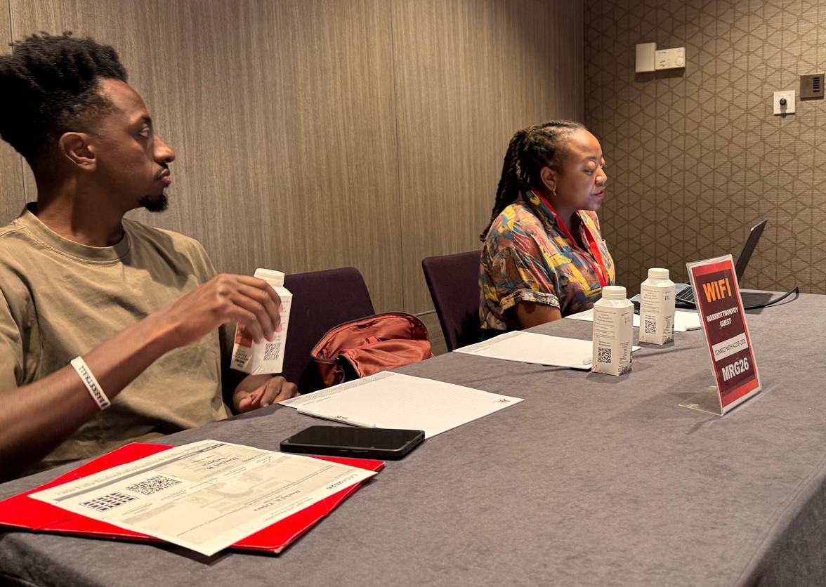 Black man at left of conference table, black woman at right of table; conference materials sitting on table.